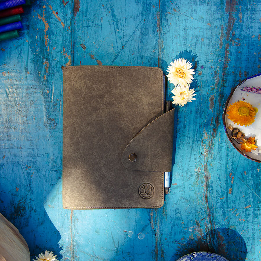 greenbook alles in einem auf einem blauen Holztisch mit geschlossener veganer Decke, 2 Blumen und ein paar Accessoires, um ihn zu verschönern