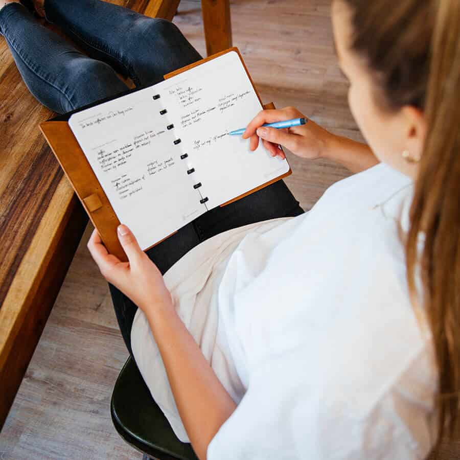 ein Model hält ein gepolstertes Whiteboard-Notizbuch auf dem Schoß, sie schreibt mit einem Stift auf die löschbaren Blätter