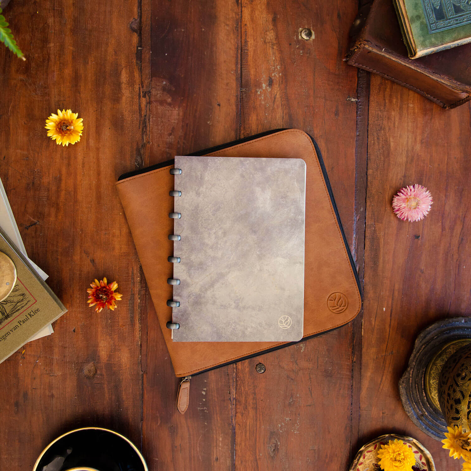 radierbares Notizbuch mit betongrauem Einband und raumgrauen Ringen und ein cognacfarbenes Arbeitsbuch, das flach auf einem antiken Holztisch liegt